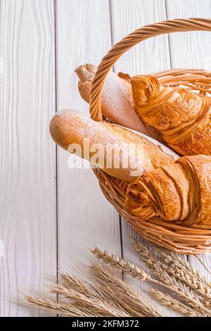 Croissants und Baguettes im Korbkorb mit Ähren aus Weizen auf weißen Holzbrettern Stockfoto