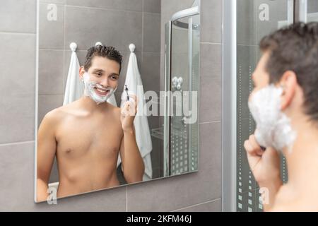 Der junge Mann Rasierprozess im Badezimmer. Der Teenager rasiert den Bart ab. Stockfoto