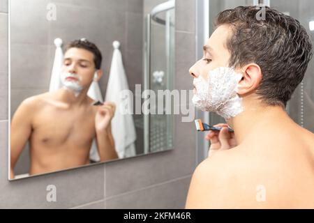 Der junge Mann Rasierprozess im Badezimmer. Der Teenager rasiert den Bart ab. Stockfoto