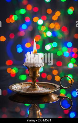 Glühende alte Kerze im Wintage-Kerzenhalter auf Spiegeloberfläche mit mehrfarbigem Bokeh Stockfoto