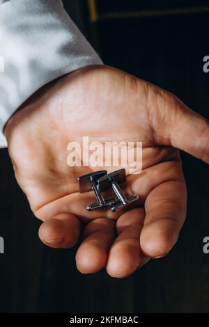 Ein Mann in einem Hemd hält modische Manschettenknöpfe in den Händen, aus nächster Nähe. Stockfoto