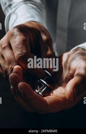 Hochzeitsmode für Männer. Nahaufnahme eines kaukasischen Mannes, der die Manschettenknöpfe in der Hand hält Stockfoto