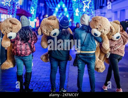 Touristen sehen die Weihnachtsdekorationen in Londons Mayfair und halten sich stolz an ihrem riesigen Kuschelspielzeug fest. Stockfoto