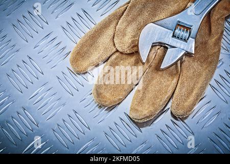 Sicherheitshandschuhe verstellbarer Schraubenschlüssel auf gerilltem Blechbaukonzept. Stockfoto