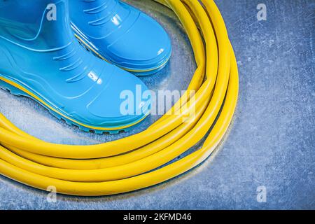 Sicherheit Gummi Stiefel Gummi Garten Wasser Rohr Spule auf metallischen Hintergrund Gartenarbeit Konzept. Stockfoto