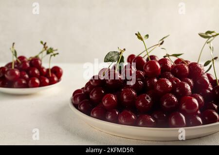 Reife Kirschen auf einem Teller auf hellem Hintergrund, leckere, süße Beerennaturprodukte ohne Pestizide Stockfoto