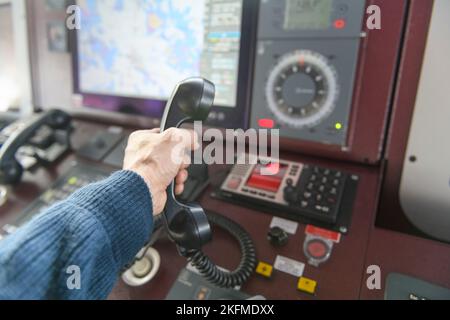 Navigationsbedienfeld und UKW-Funkgerät mit Hand. Funkkommunikation auf See. Arbeiten an der Schiffsbrücke. Stockfoto