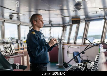 Deckoffizier mit Fernglas auf der Navigationsbrücke. Seemann an Bord des Schiffes. Gewerblicher Versand. Frachtschiff. Stockfoto