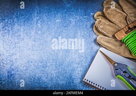 Arbeitsbuch mit weichen Twist-Krawatten für Gartenscheren und Sicherheitshandschuhen auf metallischem Hintergrund. Stockfoto