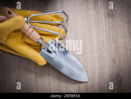 Edelstahl-Handkelle Rechen gelb Leder Arbeitshandschuhe auf Holzbrett Landwirtschaft Konzept. Stockfoto