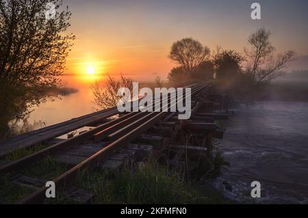 Schöner Sommermorgen. Brücke mit Schienen bei einem schönen Sonnenaufgang. Foto aufgenommen in Motkowice, Polen. Stockfoto