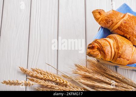 Zwei Croissants und Weizenohren auf alten weißen Holzbrettern mit Copyspace Stockfoto