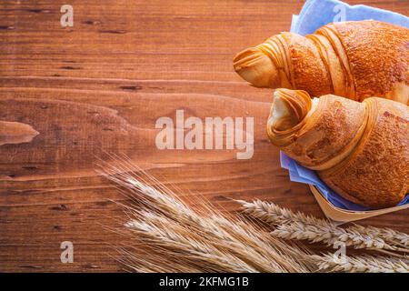 Zwei Croissants und Ähren aus Weizen auf altem Holzbrett Stockfoto