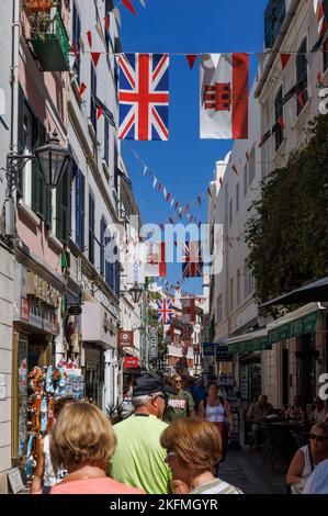 Shopper in Main Street, Gibraltar, mit der Flagge von Gibraltar und Union Jacks auf der Straße. Stockfoto