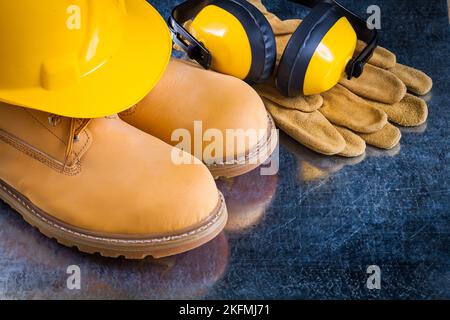 Wasserdichte Stiefel Leder Schutzhandschuhe Ohrenschützer und Bauhelm auf zerkratzten metallischen Hintergrund Konstruktionskonzept. Stockfoto