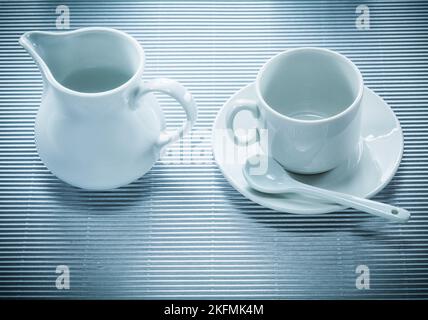 Weiße Keramik-Tasse Untertasse Teelöffel Creamer auf gestreiftem Hintergrund. Stockfoto