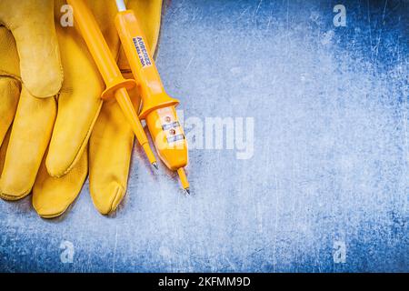 Gelbe Sicherheitshandschuhe für elektrische Tester auf metallischem Hintergrund für das Elektrizitätskonzept. Stockfoto