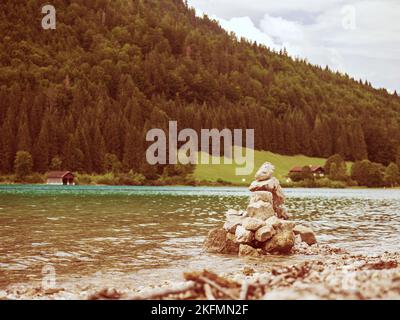 Balancierte Steine in einer Pyramide am Seewasser mit Dolomitenalpen-Spiegelung gestapelt. Gestapelte Kieselsteine am Strand Stockfoto