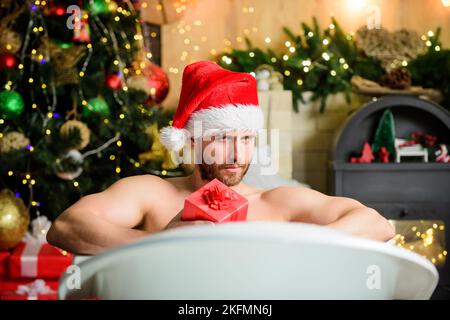 Erfreuen Sie sich. Mich verwöhnen lassen. Winterurlaub. Weihnachtskonzept. Mann, der in der Badewanne liegt, kann sich mit einer Geschenkbox entspannen. Spa und Wellness. Heißes Bad. Heißes Bad Stockfoto