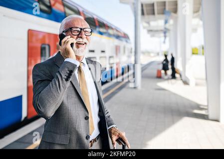 Lächelnder Unternehmer im Gespräch mit dem Smartphone. Männlicher Profi wartet mit Gepäck im Zug. Er ist in Anzug, während er in der U-Bahn oder steht Stockfoto