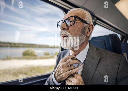 Nahaufnahme eines gestressten Geschäftsmannes, der sich während der Fahrt im Zug mit einem Herzinfarkt unwohl fühlt. Stockfoto