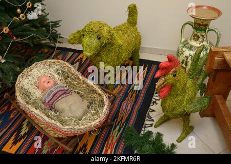 Weihnachtsgeschenke aus Stroh Spielzeug Puppe in einer Wiege, Schafe und Hahn von Weihnachtsbaum vor Neujahr platziert. Kiew, Ukraine. Stockfoto