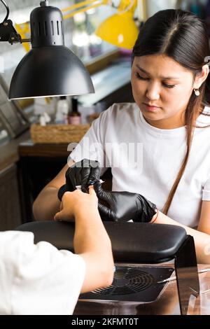 Der Manikurist behandelt den Nagel des Kunden mit einer entfettenden Flüssigkeit, um die Nägel für die Maniküre vorzubereiten und die klebrige Schicht zu entfernen. Stockfoto