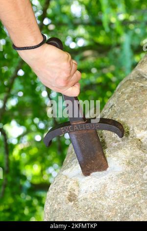 Die Hand des jungen Mannes, der gewaltsam versucht, das Schwert Excalibur zu extrahieren, steckt wie König Arthur im Felsen fest Stockfoto