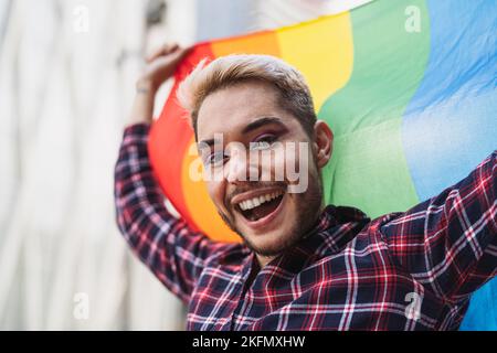 Fröhlicher schwuler Mann, der das PRIDE-Festival mit der LGBTQ-Regenbogenflagge feiert Stockfoto
