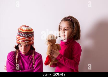 Gieriges Kinderkonzept. Beziehungen der Schwestern. Teile Spielzeuge mit Freunden. Kinder auf weißem Hintergrund spielen mit Spielzeug Stockfoto