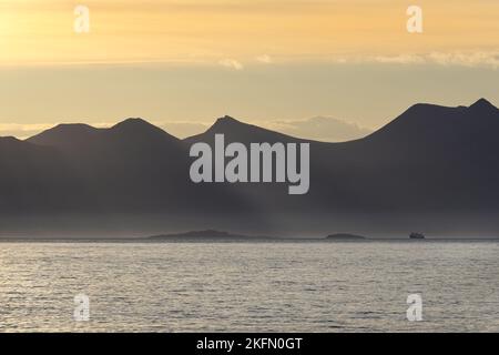 Die Cal-Mac-Fähre, die von den Bergen der Ben More Coigach Range in den Schatten gestellt wird, während das Morgenlicht die Szene von Mellon Udrigle, Wes, aus betrachtet, erhellt Stockfoto