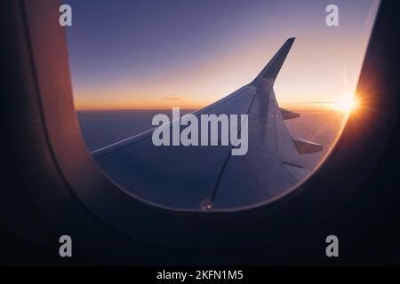 Romantischer Blick vom Flugzeugfenster über den Flügel während des wunderschönen Sonnenuntergangs. Die Sonne steht am Horizont und färbt den Himmel. Stockfoto