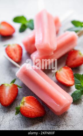 Hausgemachte gefrorene Erdbeer-Eis-Eiszapfen und frische Erdbeeren auf einem betonierten Hintergrund. Sommerdessert Stockfoto