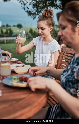 Familie mit einer Mahlzeit vom Grill während des Sommer Picknick im Freien Abendessen in einem Hausgarten. Nahaufnahme von Leuten, die an einem Tisch mit Essen und Geschirr sitzen Stockfoto