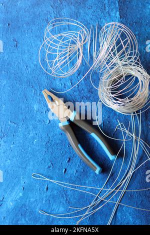 Vintage-Zange, Draht und Armierungsstahl auf blauem strukturiertem Hintergrund mit Kopierbereich. Renovierungsarbeiten im Detail. Stockfoto