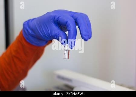Eine Hand in einem Gummihandschuh, die eine Nahaufnahme eines Fläschchens hält Stockfoto