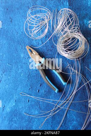 Vintage-Zange, Draht und Armierungsstahl auf blauem strukturiertem Hintergrund mit Kopierbereich. Renovierungsarbeiten im Detail. Stockfoto