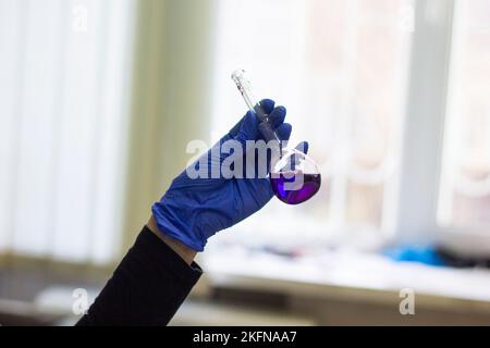 Eine Durchstechflasche mit einer violetten Lösung wird mit Handschuhen in der Hand gehalten Stockfoto