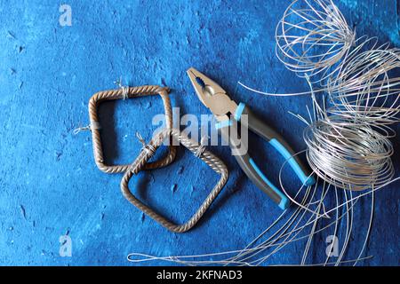 Vintage-Zange, Draht und Armierungsstahl auf blauem strukturiertem Hintergrund mit Kopierbereich. Renovierungsarbeiten im Detail. Stockfoto