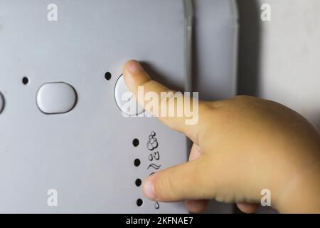 Die Hand eines Kindes drückt einen Knopf an einer Waschmaschine Stockfoto