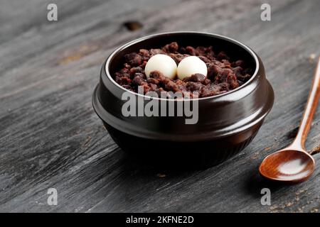 Patjuk, korean Red Bean Porridge mit Reiskuchen auf der Oberseite. Serviert auf schwarzem Holztisch Stockfoto