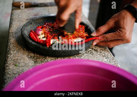 Nahhand einer Person, die den Chili-Knoblauch und die Zwiebel reibt. Zubereitete traditionelle indonesische Sauce oder Gewürze namens Sambal Stockfoto