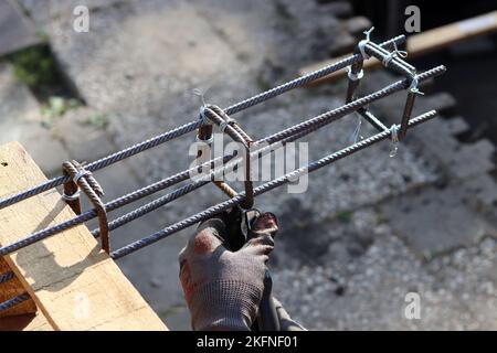 Nahaufnahme eines Mannes, der eine Zange hält. Man arbeitet mit Bewehrungsstahl. Bauarbeiten im Detail. Stockfoto