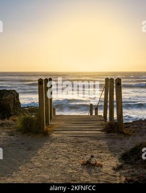 Eine vertikale Aufnahme über einer hölzernen Treppe zum Meer während der goldenen Stunde in Italien Stockfoto