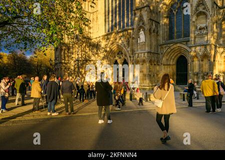 Besucher, die eine neue geschnitzte Elizabeth 2-Statue auf einer Nische (in Strumpfroben) vor dem York Minster, West Front, North Yorkshire, England, sehen Stockfoto