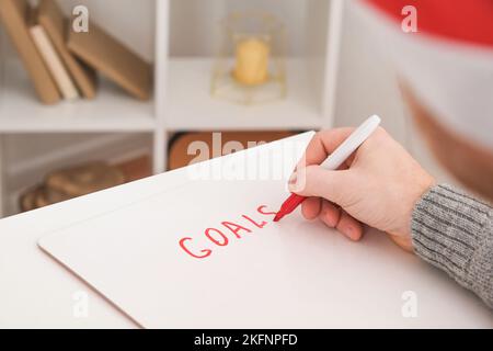 Ein Mann schreibt Marker Board weißen Tisch mit Weihnachtsdekor Ziele und Pläne für das neue Jahr und Weihnachten. Ziele für das neue Jahr auf einem Marker-Board geschrieben. Wünsche und Ziele für das neue Jahr 2023. Stockfoto