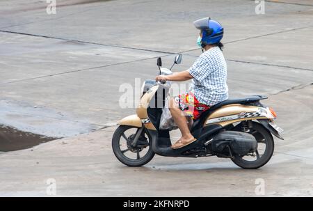 SAMUT PRAKAN, THAILAND, SEP 26 2022, Eine Frau mit Gesichtsmaske fährt ein Motorrad Stockfoto