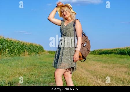 Wunderschöne Frau in einem Weizenfeld auf einem Sonnenuntergang Hintergrund. Ein modisches Mädchen mit langen Haaren freut sich, lacht, genießt Leben und Sommer, Natur, Glück. Stockfoto