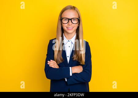 Foto von optimistisch liebenswert smart schulmädchen mit geraden Frisur tragen blauen Blazer Hände gefaltet isoliert auf gelbem Hintergrund Stockfoto