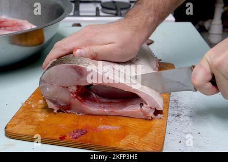 Der Mensch bereitet frischen Silberkarpfen zu. Schneidet es in Steaks mit einem Messer. Hausmannskost-Konzept. Stockfoto